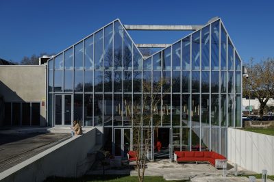 Área externa com um deck de madeira clara e cadeiras minimalistas ao lado de um pequeno lago com pedras e plantas aquáticas. O design reflete a harmonia entre natureza e arquitetura, típico do estilo japonês.