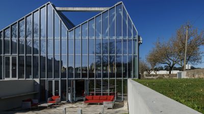 Pátio externo com uma fonte de água em pedra ao centro, cercada por vegetação japonesa e um caminho de madeira. O espaço reflete a fusão entre design moderno e a estética zen, promovendo calma e relaxamento.