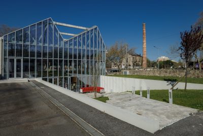 Zona exterior com bancos de madeira em um jardim com árvores e bambus, criando um ambiente de descanso inspirado em jardins japoneses. A iluminação suave e o uso de materiais naturais reforçam o toque moderno e tranquilo.