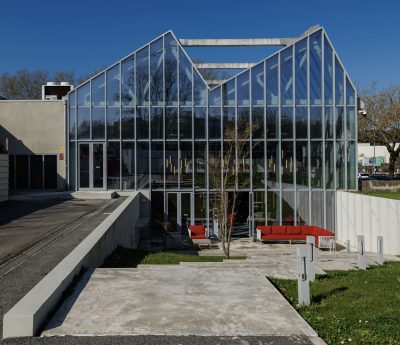 Área exterior com grandes painéis de vidro conectando o interior ao jardim zen. Pedras, plantas baixas e lanternas de pedra criam um ambiente relaxante, destacando o minimalismo japonês em um contexto contemporâneo.