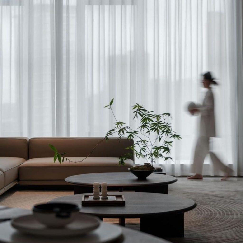 Sala minimalista em tons neutros, criada através de um design de interiores que privilegia o bem estar e reforça a saúde e bem estar, com luz suave e elementos naturais que promovem calma. A presença de plantas e a fluidez do espaço apoiam a saúde mental e intensificam o bem estar, mostrando como o design de interiores pode contribuir para a saúde e bem estar e favorecer um ambiente que nutre a saúde mental.