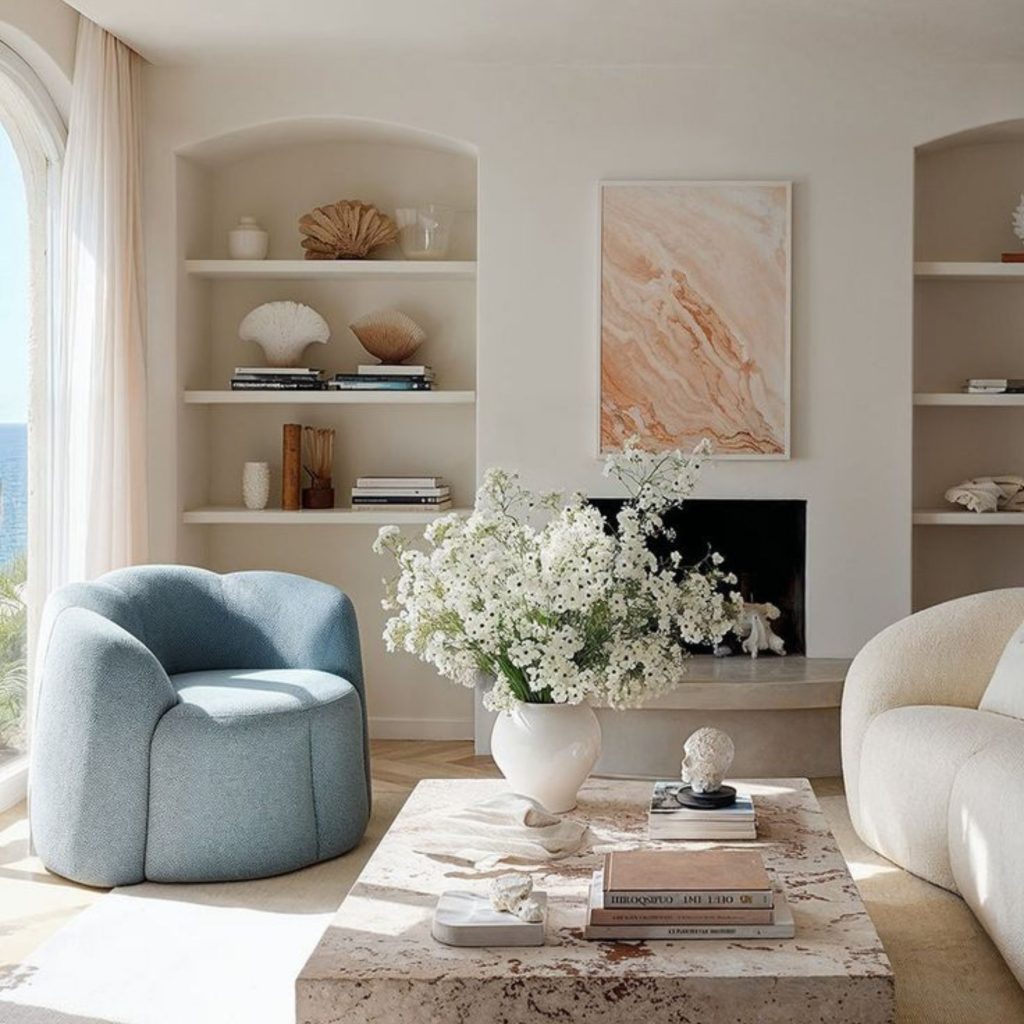 Sala luminosa com vista costeira, decorada em tons suaves que exploram a cor pastel para criar um ambiente sereno dentro de um design de interiores contemporâneo. A poltrona azul-clara, o sofá curvo creme e os detalhes naturais reforçam uma paleta de cores pastel equilibrada. O espaço evidencia como o design de interiores pode integrar cor pastel de forma subtil, enquanto a paleta de cores pastel presente nas paredes, têxteis e objetos decorativos transmite leveza e harmonia.