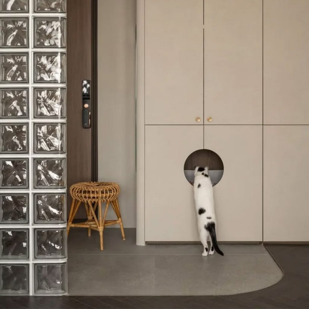Um gato investiga uma abertura integrada no armário, sobre um pavimento resistente à humidade e fácil de limpar, ideal para uma casa partilhada com animais de estimação. A transição entre madeira e cerâmica reforça a lógica funcional do design de interiores, mantendo a decoração minimalista e coerente com um estilo pet‑friendly. Neste espaço, a casa responde às necessidades dos animais de estimação, oferecendo materiais duráveis e superfícies práticas, enquanto o design de interiores e a decoração asseguram um ambiente equilibrado, elegante e plenamente pet‑friendly.