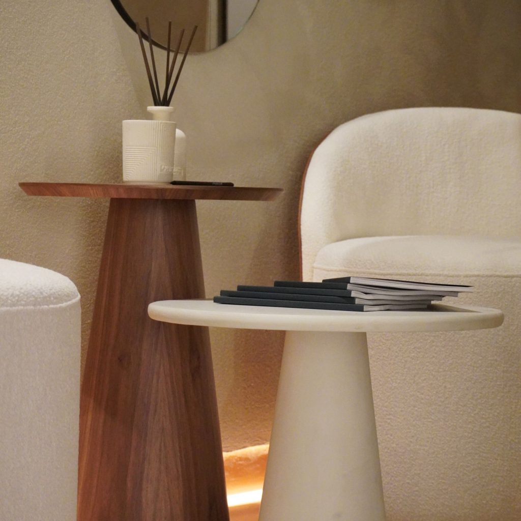 Detalhe de mesas laterais esculturais e cadeira estofada num espaço minimalista que evoca o espírito do salone del mobile 2026 e das suas tendências. A paleta neutra e as formas orgânicas revelam como o salone del mobile 2026 continua a moldar o design de interiores, reforçando tendências que valorizam materiais naturais e proporções equilibradas no design de interiores.