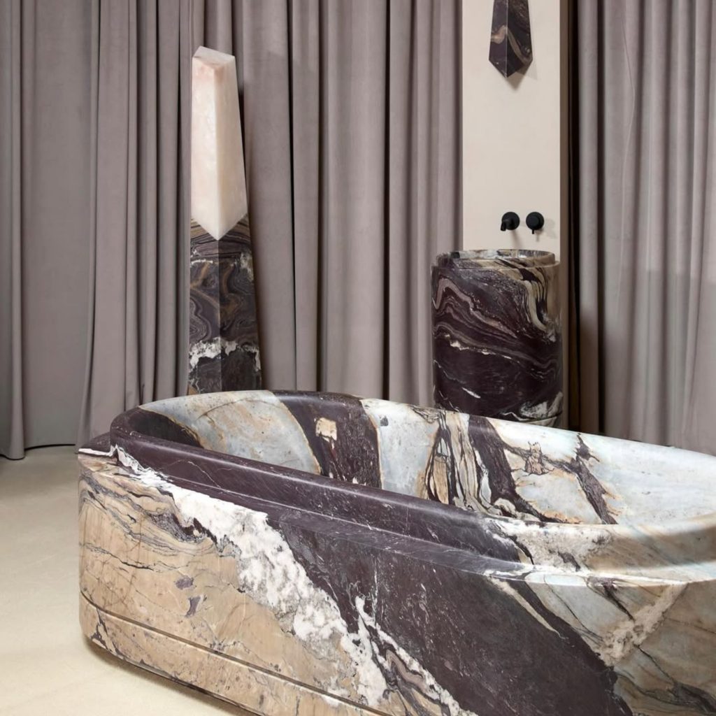Casa de banho com banheira escultórica e coluna decorativa, evocando o espírito do salone del mobile 2026 e das suas tendências. A presença da pedra natural mostra como o salone del mobile 2026 continua a influenciar o design de interiores, reforçando tendências que valorizam formas escultóricas e materiais expressivos no design de interiores.