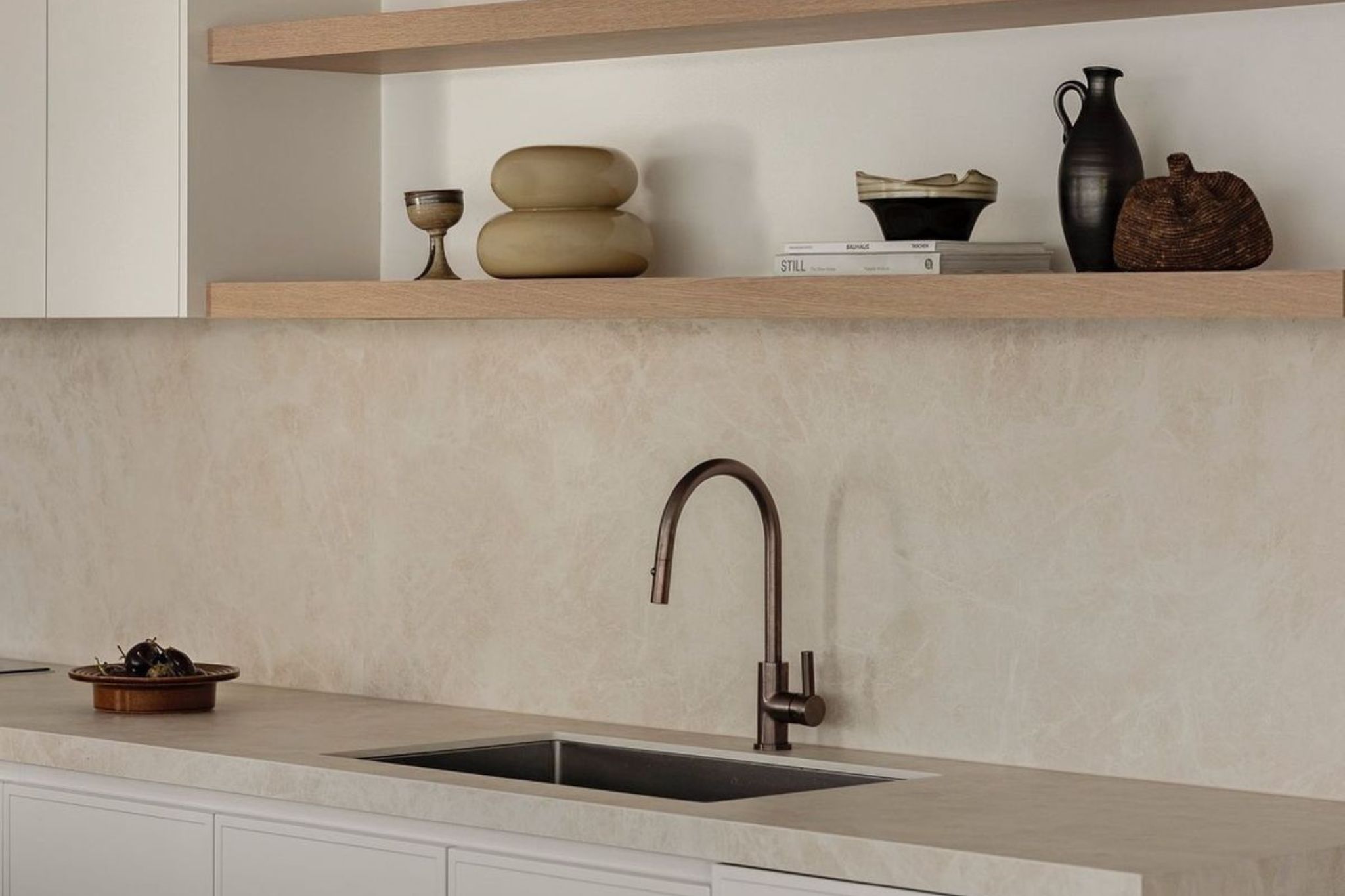 Cozinha minimalista com prateleiras de madeira e objetos decorativos que dialogam com utensílios de cozinha num ambiente típico de cozinhas modernas; composição neutra onde o lavatório e os utensílios de cozinha se integram em cozinhas modernas orientadas pelo design de interiores, reforçando a simplicidade e a presença subtil do design de interiores