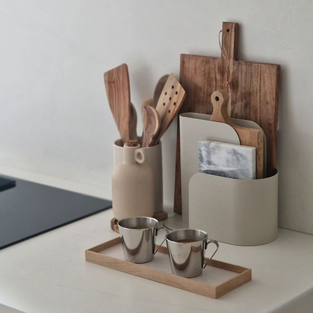 Composição organizada onde utensílios de cozinha decorativos são reunidos num único ponto da bancada, criando ordem visual típica de cozinhas modernas; a disposição dos utensílios de cozinha junto a tábuas e recipientes reforça a estética das cozinhas modernas e a coerência do design de interiores, integrando o design de interiores de forma subtil e harmoniosa.