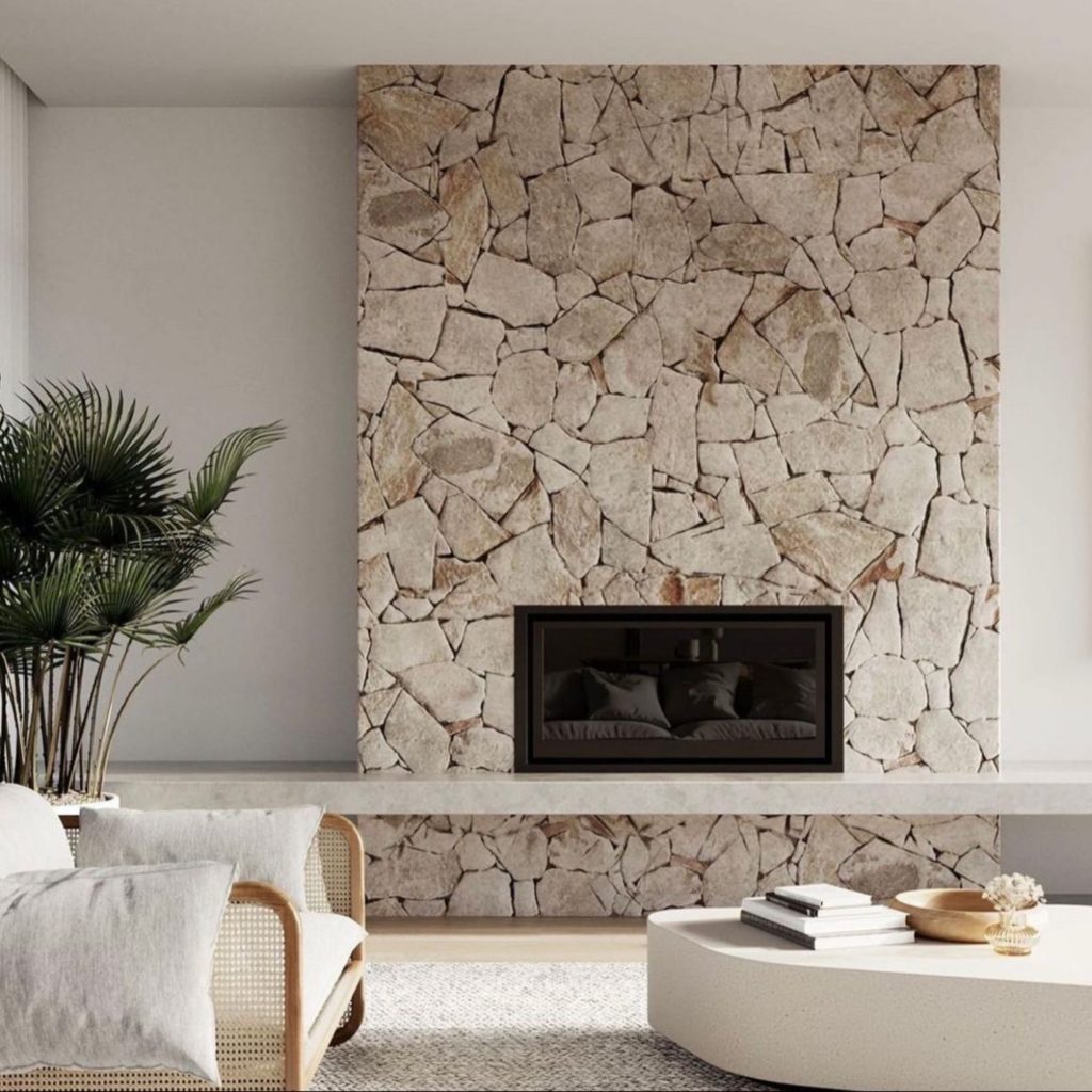 A parede em pedra natural e a mesa curva criam uma decoração que combina textura, luz e matéria para despertar emoções de conforto e recolhimento. A presença da lareira reforça a dimensão sensorial do espaço, revelando como a arquitetura organiza atmosferas e regula a perceção do ambiente. Cada elemento contribui para uma decoração intencional, onde as emoções emergem da relação entre materiais naturais e proporção, refletindo uma abordagem de arquitetura que privilegia equilíbrio, silêncio e profundidade visual.