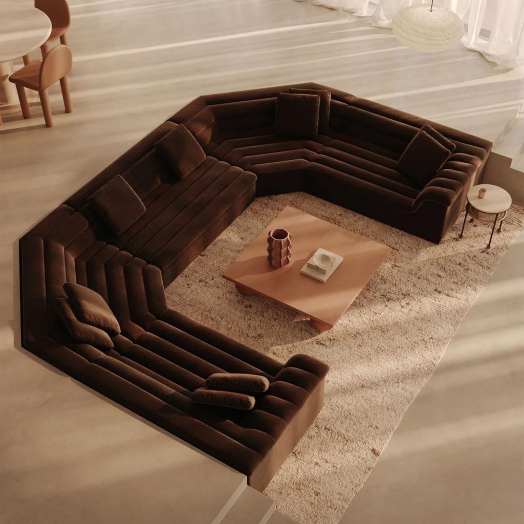 A sala apresenta uma decoração que privilegia formas envolventes e tons quentes, criando um ambiente que desperta emoções de conforto e proximidade. A configuração modular do sofá e a mesa central escultórica revelam a intenção da arquitetura em organizar o espaço através de fluidez e convivência. A coerência da decoração reforça a ligação emocional ao ambiente, permitindo que as emoções se expressem de forma natural. Cada detalhe traduz uma abordagem de arquitetura sensorial, onde luz, textura e proporção se articulam para criar uma atmosfera acolhedora, e onde as emoções se alinham com a intenção da arquitetura