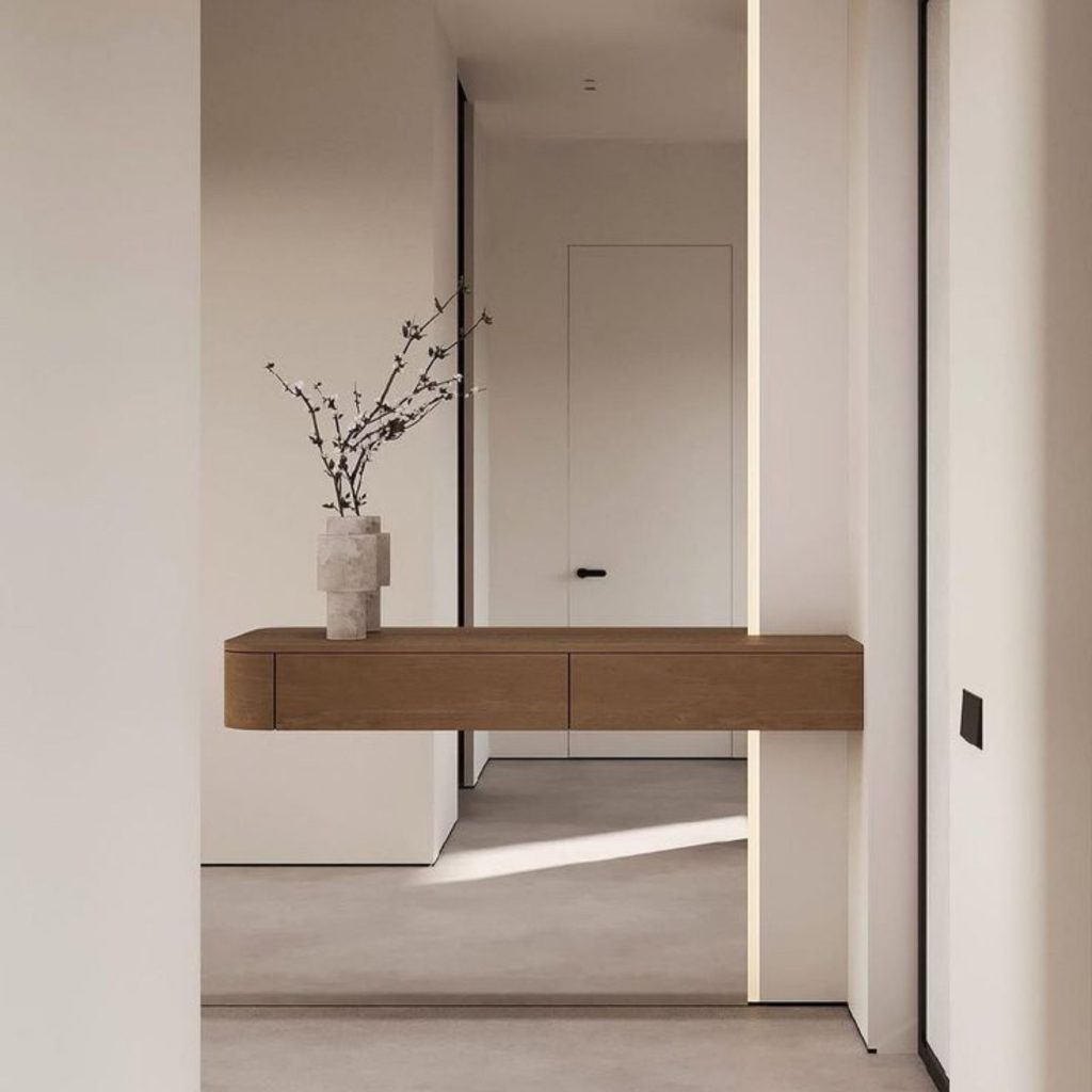 Hall contemporâneo onde superfícies livres reforçam uma decoração depurada, permitindo que as emoções se expressem com naturalidade num ambiente silencioso. A consola suspensa e o vaso escultórico revelam a intenção da arquitetura em criar leveza visual, mostrando como a decoração organiza o espaço através de proporção e contenção. A composição traduz uma abordagem sensorial, onde as emoções são moldadas pela clareza espacial e onde a arquitetura se articula com uma decoração que privilegia ordem, luz e equilíbrio, despertando emoções de tranquilidade.