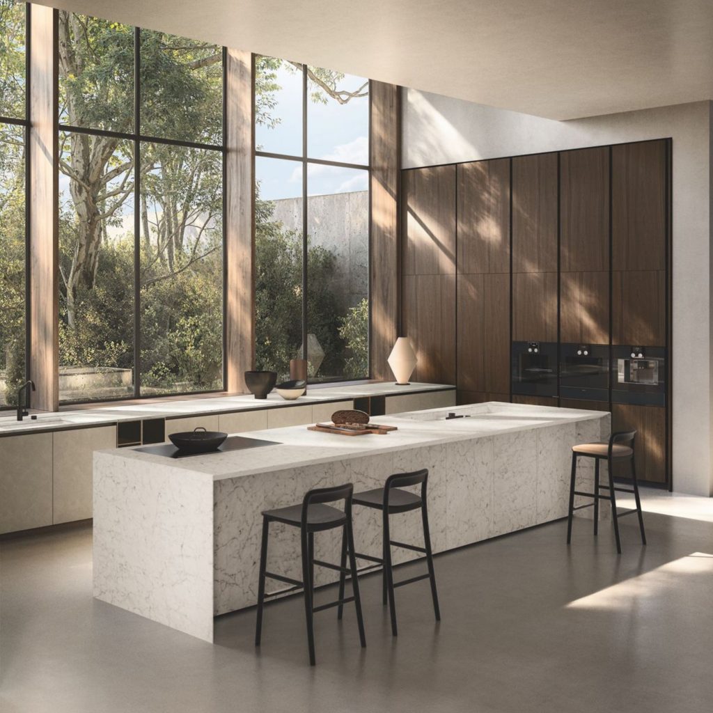 Uma cozinha contemporânea onde os paineis acústicos ajudam a controlar o eco natural do espaço, suavizando o som e reduzindo fenómenos acústicos provocados por superfícies rígidas. A presença de espuma acústica integrada discretamente reforça a insonorização acústica, permitindo que o ambiente mantenha clareza mesmo com volumes elevados de som. A luz natural evidencia como os paineis acústicos estabilizam fenómenos acústicos, enquanto a espuma acústica contribui para uma insonorização acústica eficaz, reduzindo o eco e equilibrando o som em toda a área.