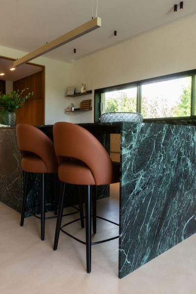 Cozinha moderna com ilha revestida a pedra, acompanhada por bancos altos que estruturam a área de refeições. A luz natural valoriza a cozinha moderna enquanto os bancos altos reforçam a funcionalidade da cozinha moderna com ilha. Um ambiente contemporâneo onde a combinação de materiais destaca os bancos altos e a presença marcante da cozinha moderna e da cozinha moderna com ilha.