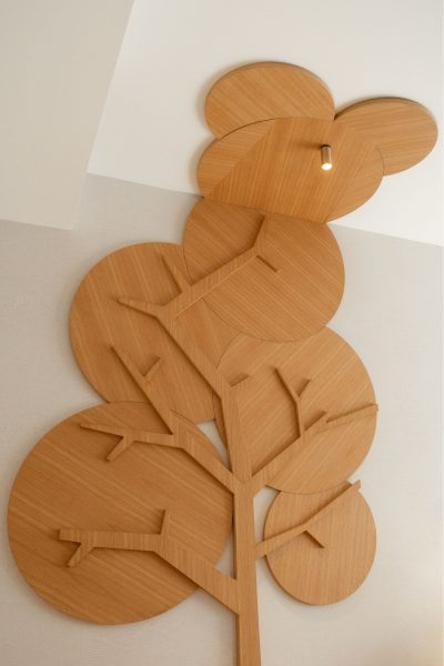 Painel decorativo em madeira em forma de árvore aplicado à parede de um quarto de criança. A decoração destaca um elemento escultórico que reforça a decoração do espaço e acrescenta personalidade à decoração. O design de interiores privilegia materiais naturais, enquanto o design de interiores cria uma linguagem lúdica e o design de interiores mantém uma estética contemporânea. Este quarto de criança foi pensado para estimular a imaginação, sendo um quarto de criança acolhedor, um quarto de criança funcional e um quarto de criança integrado numa proposta elegante.