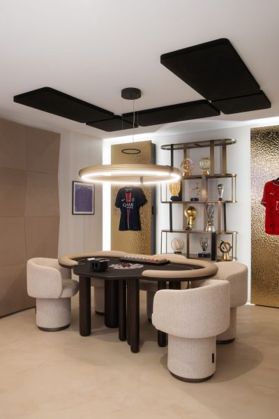 Vista ampla de uma sala de jogos com mesa de poker, iluminação suspensa circular, painéis acústicos e exposição de troféus. A decoração cria um ambiente exclusivo, a decoração reforça o carácter personalizado do espaço e a decoração estabelece uma linguagem contemporânea. O design de interiores organiza cuidadosamente cada elemento, o design de interiores valoriza a experiência dos utilizadores e o design de interiores promove conforto visual. Esta sala de jogos integra um projeto de design de interiores de luxo, onde o projeto de design de interiores de luxo combina lazer e sofisticação e o projeto de design de interiores de luxo responde a um estilo de vida exigente dentro da sala de jogos.