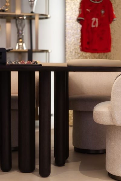 Mesa de jogo em madeira escura com cadeiras estofadas em tons claros, integrada numa sala de jogos sofisticada. A decoração valoriza o contraste entre materiais, a decoração reforça a atmosfera exclusiva do espaço e a decoração contribui para uma experiência envolvente. O design de interiores privilegia formas esculturais, o design de interiores equilibra conforto e funcionalidade e o design de interiores evidencia atenção ao detalhe. Esta sala de jogos foi concebida como um projeto de design de interiores de luxo, onde o projeto de design de interiores de luxo se reflete na seleção de peças e onde o projeto de design de interiores de luxo cria uma identidade única para a sala de jogos.