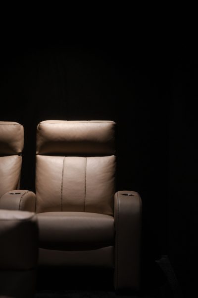 Pormenor de uma poltrona reclinável em pele integrada num elegante cinema em casa. O projeto de design de interiores evidencia a qualidade dos materiais, o projeto de design de interiores aposta na ergonomia e o projeto de design de interiores cria condições ideais para uma experiência confortável. Este cinema em casa foi pensado para proporcionar momentos de lazer com o máximo conforto, reforçando o carácter exclusivo do cinema em casa.