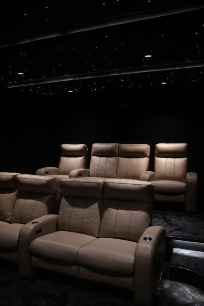 Poltronas reclináveis em pele organizadas em diferentes níveis sob um teto estrelado num exclusivo cinema em casa. O projeto de design de interiores privilegia o conforto durante longas sessões de visualização, enquanto o projeto de design de interiores recorre a iluminação discreta para reforçar a atmosfera cinematográfica. A conceção deste cinema em casa valoriza a experiência imersiva e transforma o espaço num verdadeiro refúgio dedicado ao entretenimento. Neste cinema em casa, o projeto de design de interiores combina tecnologia, conforto e sofisticação.