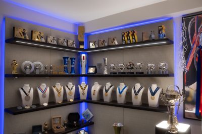 Exposição de troféus, medalhas e objetos de coleção organizados em estantes iluminadas num espaço totalmente dedicado à paixão pelo desporto. A decoração valoriza cada conquista, a decoração transforma recordações em elementos de destaque e a decoração cria uma narrativa visual única. A personalização está presente em cada detalhe, a personalização reflete a história do proprietário e a personalização confere identidade ao ambiente. Este projeto de design de interiores foi concebido para expor uma coleção exclusiva, enquanto o projeto de design de interiores organiza as peças de forma elegante e o projeto de design de interiores reforça a experiência do espaço. Integrado num projeto de design de interiores de luxo, este ambiente demonstra como um projeto de design de interiores de luxo pode combinar funcionalidade e emoção, sendo um verdadeiro projeto de design de interiores de luxo à medida do cliente.