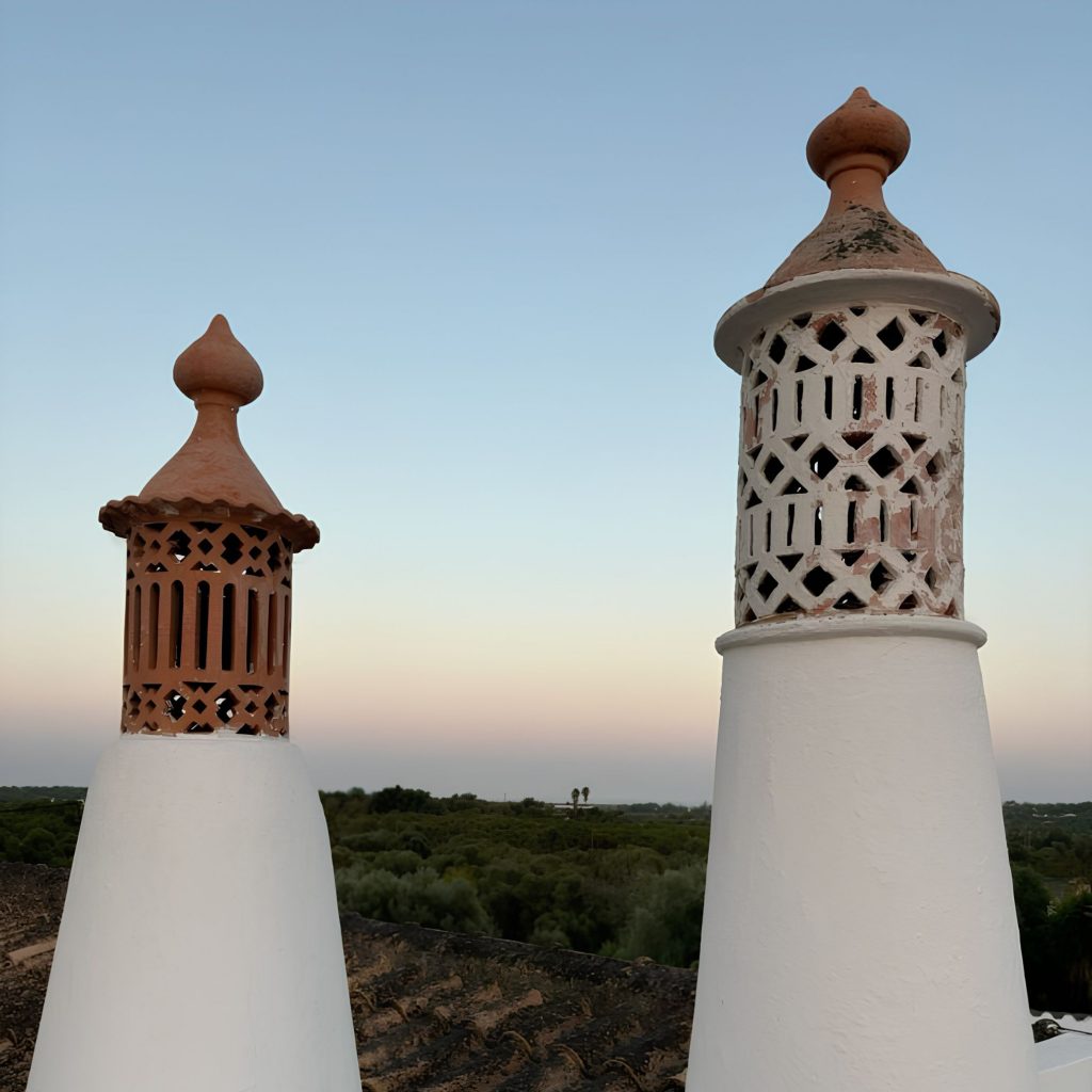 Chaminés tradicionais que evocam a identidade de uma casa algarvia, alinhadas com o espírito das casas de férias no algarve e com a estética das Casas do algarve, refletindo o carácter das Casas no algarve e sugerindo atmosferas de decoração de verão que dialogam com princípios de design de interiores; Os recortes em barro reforçam a presença de uma casa algarvia, articulando elementos das casas de férias no algarve com referências às Casas do algarve, criando continuidade com o estilo das Casas no algarve e com a linguagem de decoração de verão aplicada ao design de interiores; A luz quente intensifica a vibração de uma casa algarvia, evocando o ambiente das casas de férias no algarve e a tradição das Casas do algarve, alinhando-se com o conforto das Casas no algarve e com a estética descontraída da decoração de verão que inspira o design de interiores; A paisagem ao fundo reforça novamente a imagem de uma casa algarvia, remetendo para o ambiente das casas de férias no algarve e para os materiais das Casas do algarve, criando paralelos com o carácter das Casas no algarve e com os detalhes de decoração de verão que moldam o design de interiores; O enquadramento final celebra a autenticidade de uma casa algarvia, a atmosfera das casas de férias no algarve, a estética das Casas do algarve, o estilo das Casas no algarve, a vibração da decoração de verão e a inspiração contínua do design de interiores.