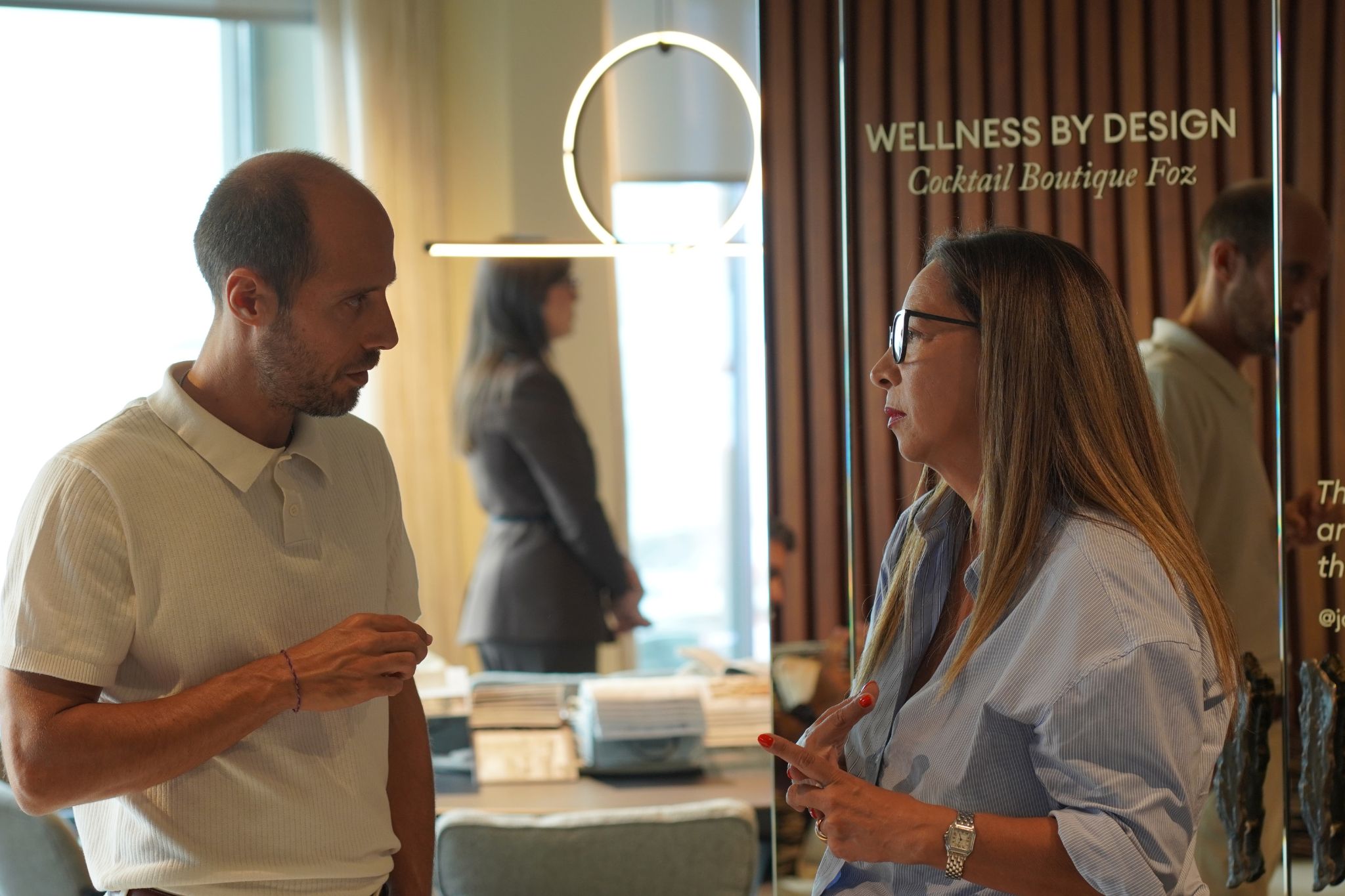 Fotografia de duas pessoas a conversar num evento de interior design, apresentando ideias de decoração aplicáveis a espaços como a casa de banho, num contexto que remete para o bem-estar e skincare.