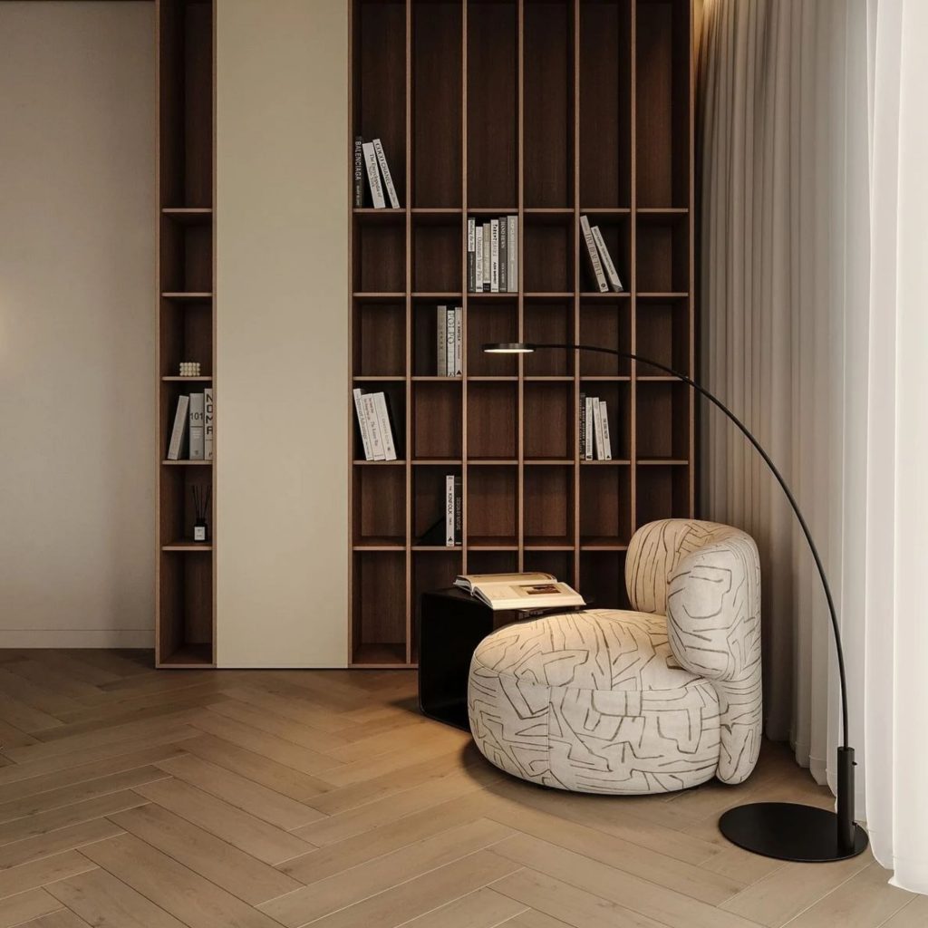 Espaço de biblioteca em casa com alta estante em nichos de madeira escura com estantes para livros, um cadeirão moderno estofado e candeeiro curvo num projeto de design de interiores e decoração sofisticado.