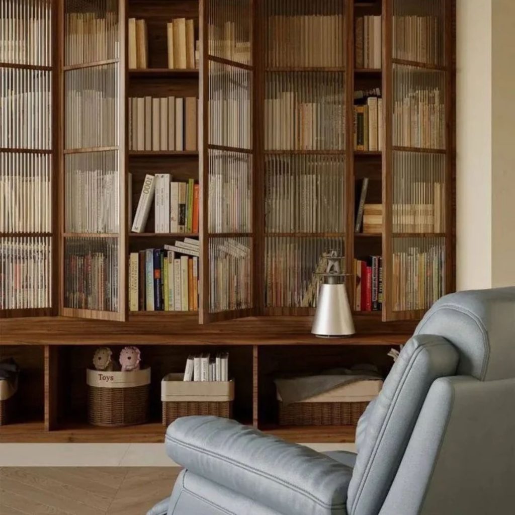 Biblioteca em casa elegante com cadeirão de leitura em primeiro plano, em frente a uma estante com portas de vidro canelado e práticas estantes para livros, unindo arrumação, decoração cuidada e design de interiores sofisticado.